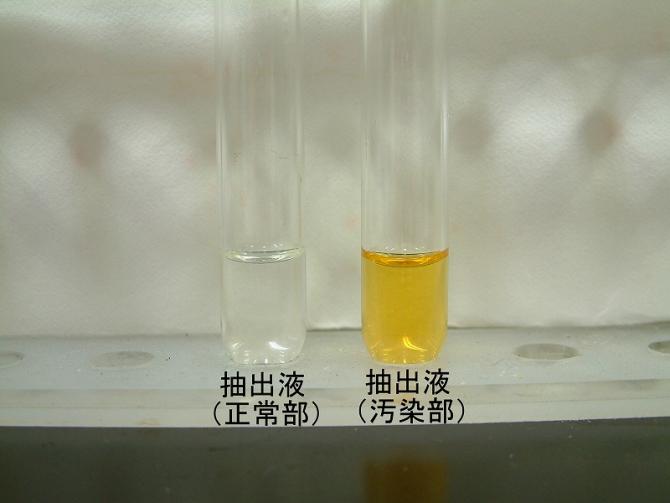 正常部と汚染部の抽出液を比較する写真。正常部無色透明。変色部褐色